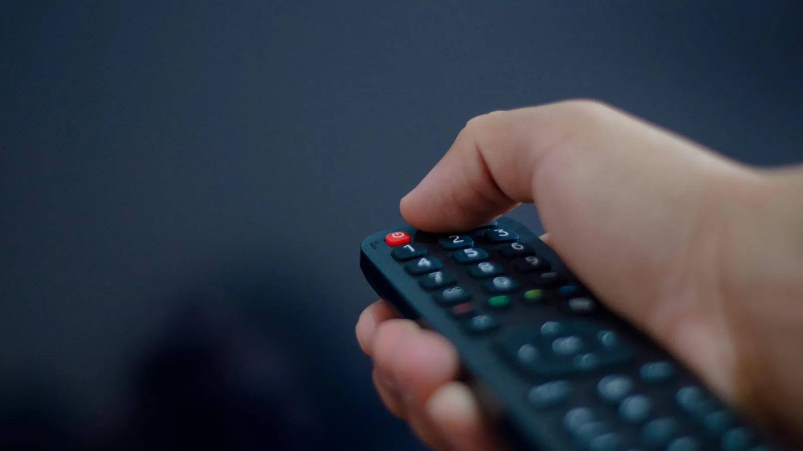 Télécommande pour téléviseur tenue en main droite sur fond sombre flou, illustration du reportage TF1 sur le réseau ORIZONS Après-vie